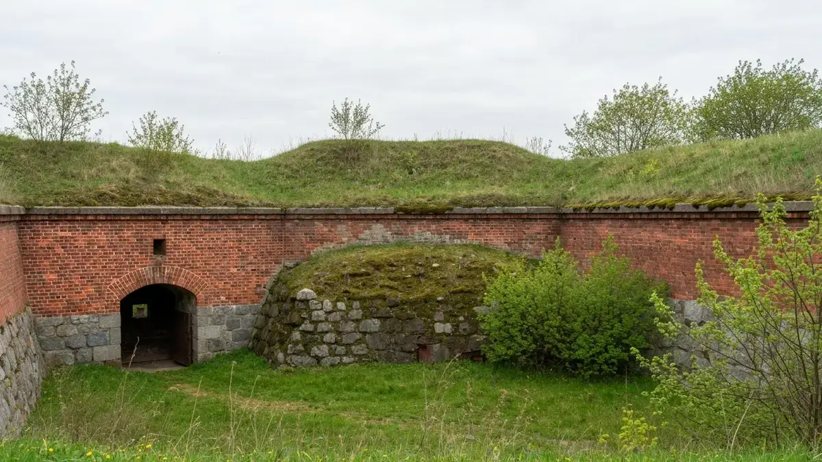 Opuszczony Fort XV w Toruniu z ceglaną ścianą, ziemnym wałem i zaroślami